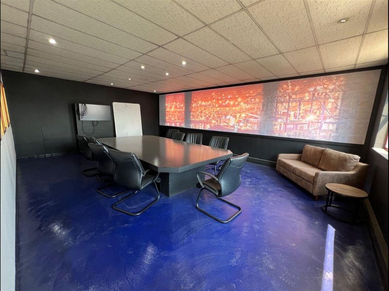 A functional office space featuring a suspended ceiling with recessed lighting, dark painted walls, and a durable blue epoxy floor finish.