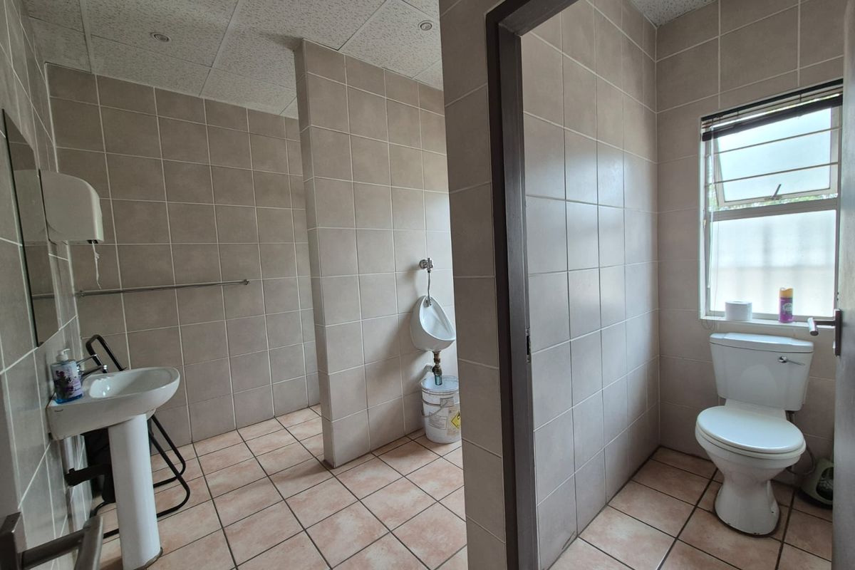Commercial restroom facility featuring tiled walls and flooring, equipped with a pedestal sink, a wall-mounted urinal, and a private toilet cubicle.