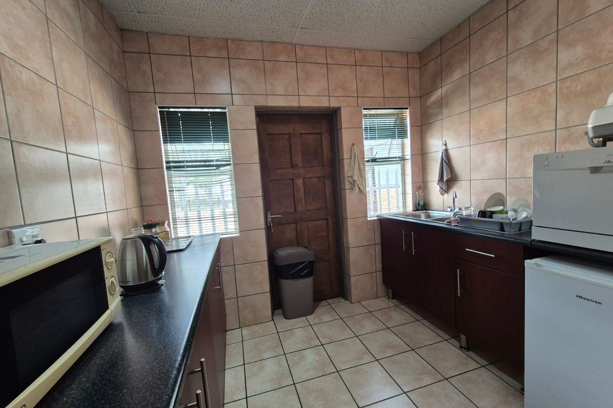 Functional kitchen area featuring dark cabinetry, tiled walls and flooring, and dual windows providing natural light.