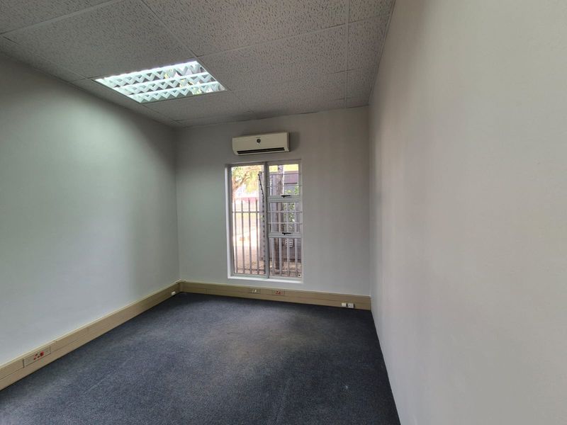 A clean, empty office space featuring a suspended ceiling, recessed lighting, wall-mounted air conditioning, and carpeted flooring with integrated skirting trunking.