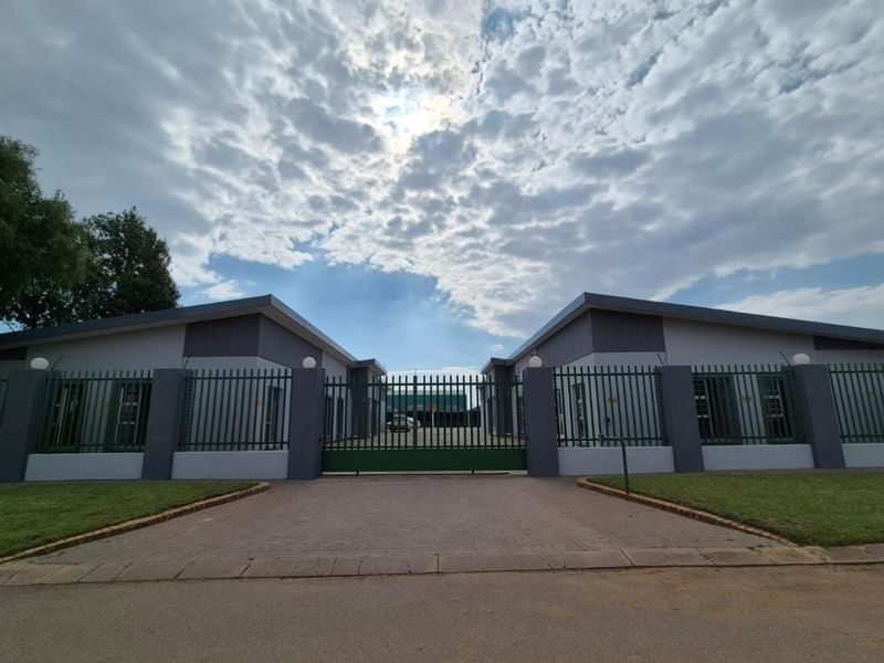 Front exterior view of a commercial property featuring a paved driveway, secure steel gate, and perimeter wall with electric fencing.