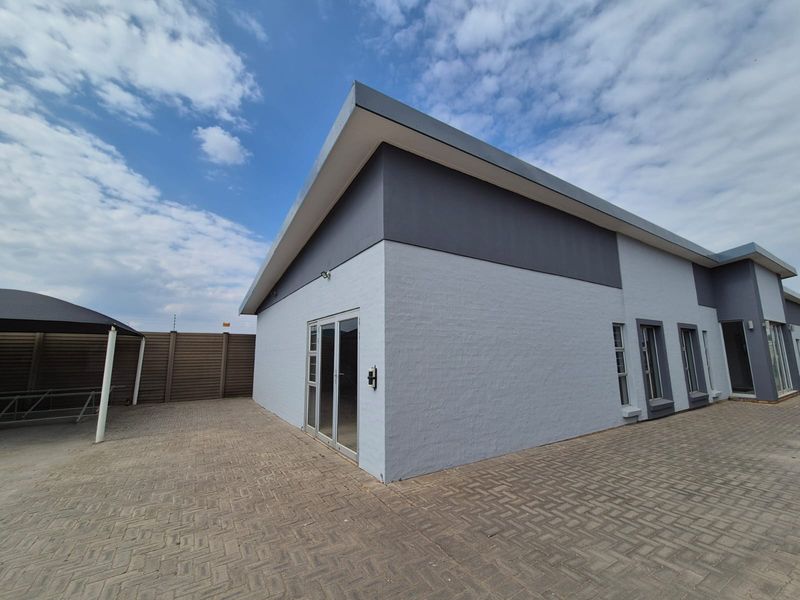 Rear exterior view of a modern commercial building featuring grey painted brickwork, aluminium framed windows and doors, and a paved courtyard area.