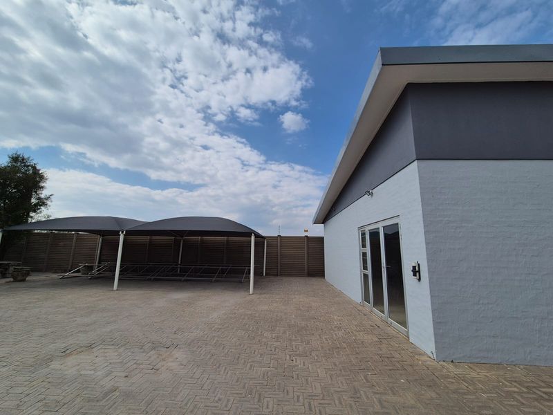 Rear exterior view featuring a paved courtyard, shade cloth carport structure, and a modern building facade with glass sliding door access.