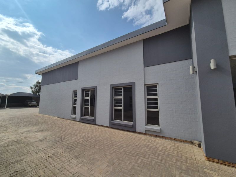 A well-maintained rear exterior view of the business property featuring a paved driveway and modern grey painted brick facade with aluminium windows.