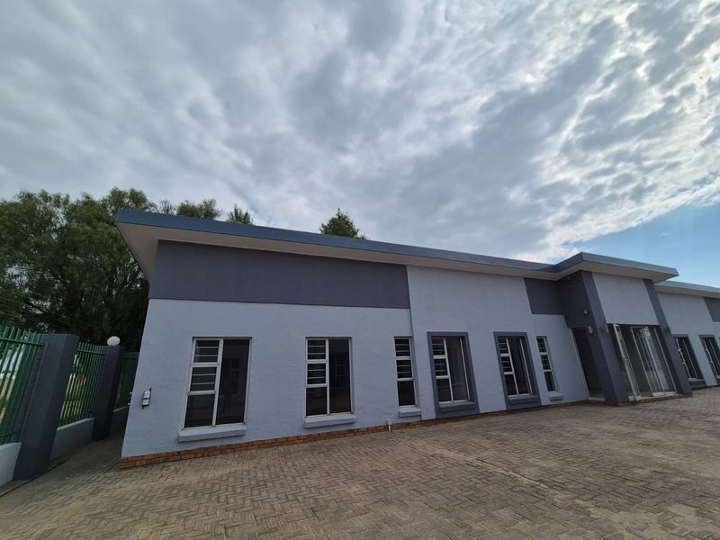 Front exterior view of a modern commercial building featuring a paved driveway, clean painted facade, and secure metal fencing.