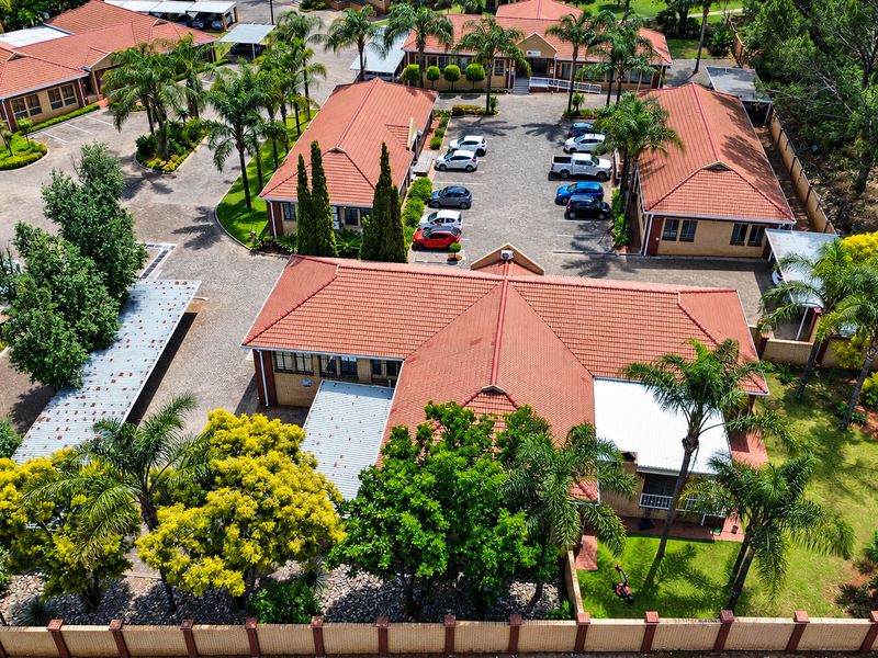 Aerial view of an office park complex featuring multiple buildings with tiled roofs, paved parking areas, and established landscaped grounds.