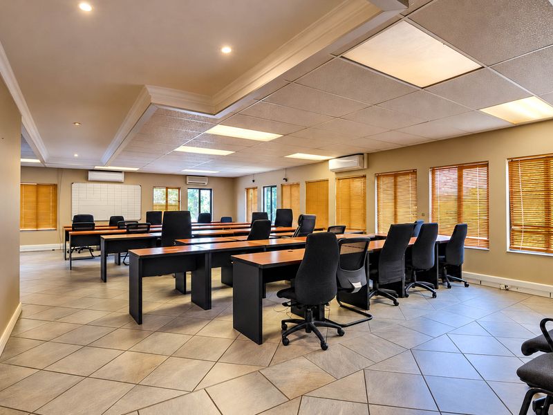 Spacious office area featuring tiled flooring, suspended ceiling with recessed lighting, multiple split-system air conditioning units, and large windows with venetian blinds.