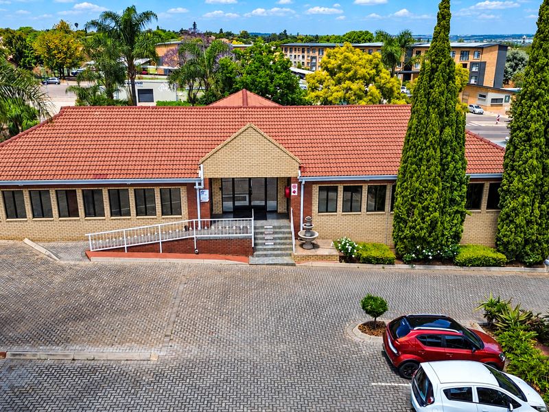 Aerial view of a well-maintained office building featuring a terracotta tile roof, brick facade, paved driveway, and accessible ramp entrance.