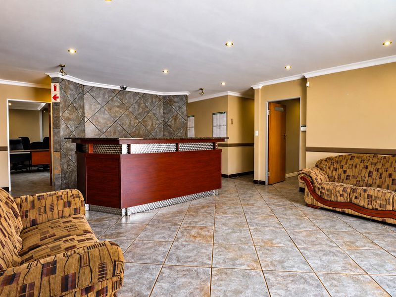 A professional office reception area featuring a built-in wooden reception desk, stone-tiled feature wall, and neutral tiled flooring with recessed lighting.