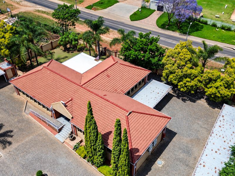Aerial view of the office property featuring a tiled roof, extensive paved parking areas, covered parking bays, and established garden landscaping.