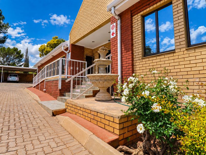 Front exterior view of the office building featuring brick masonry, paved driveway, covered parking bays, and accessible entrance steps with metal railings.