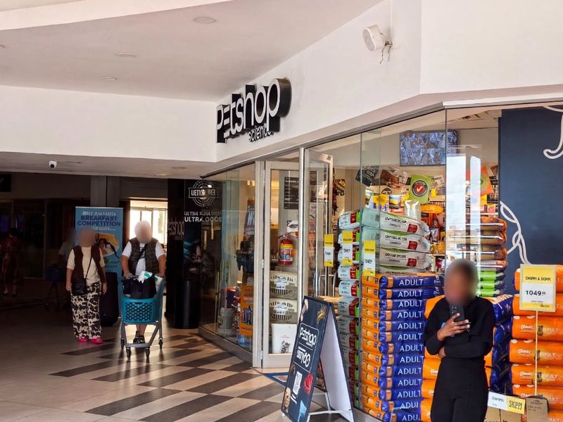 A retail storefront entrance featuring a glass facade, tiled flooring, and recessed lighting within a shopping center corridor.