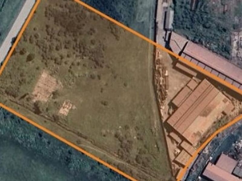 Aerial view of a commercial vacant land plot featuring an existing industrial structure and open grass area with clear boundary markings.