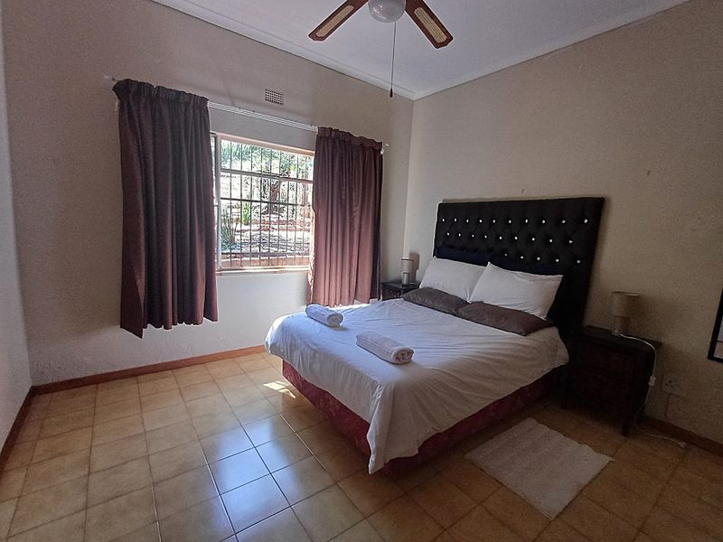A functional bedroom featuring tiled flooring, a ceiling fan, and a window fitted with security bars.