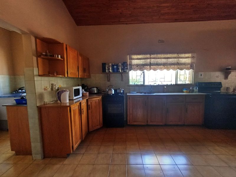 Spacious farm-style kitchen featuring wooden cabinetry, tiled flooring, built-in oven, and an exposed timber ceiling, offering a functional layout with ample storage space.