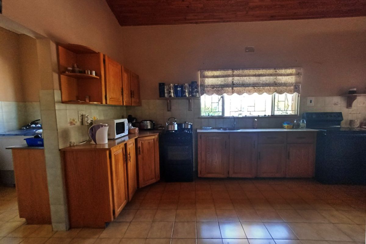Spacious farm-style kitchen featuring wooden cabinetry, tiled flooring, built-in oven, and an exposed timber ceiling, offering a functional layout with ample storage space.
