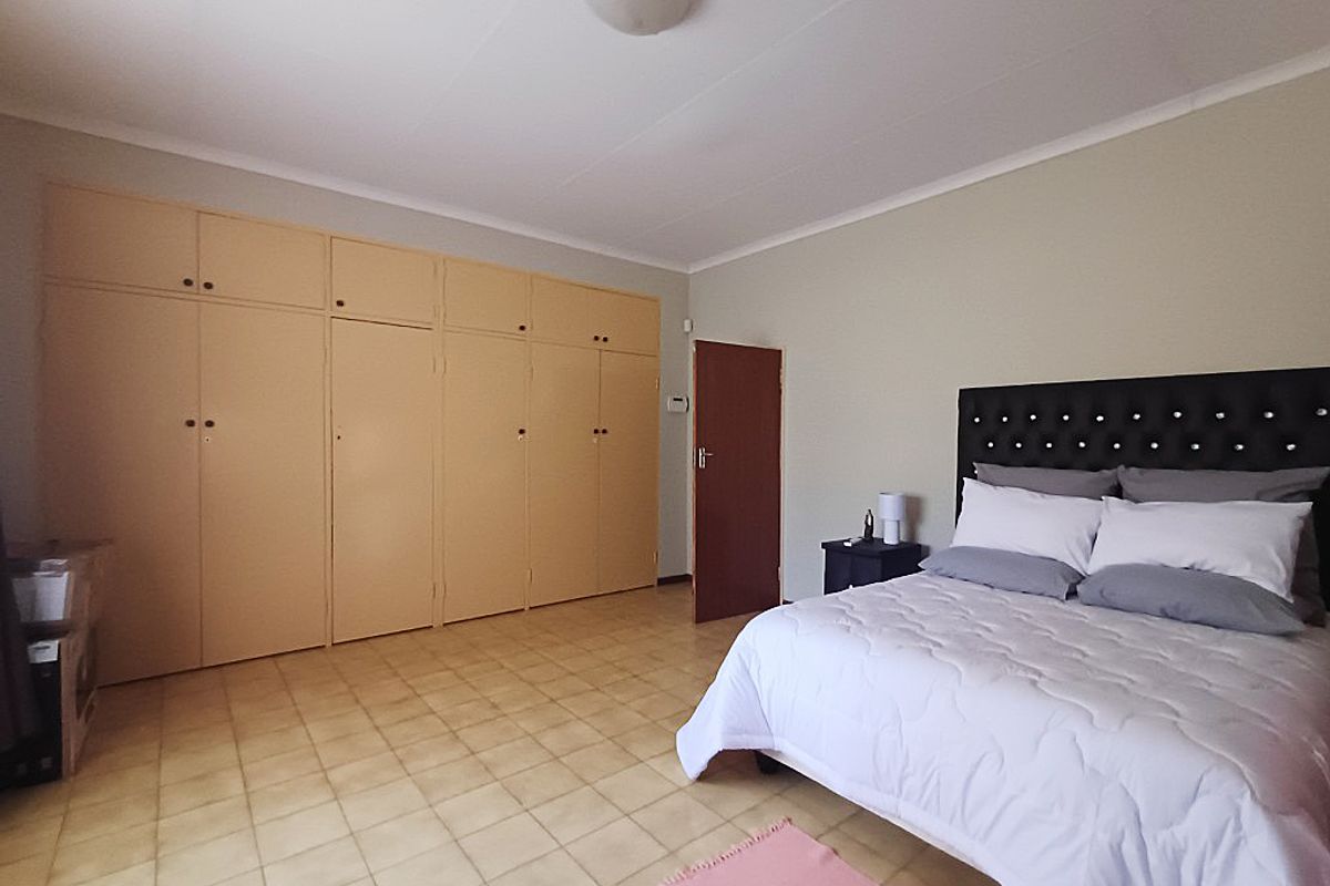 Spacious bedroom featuring extensive built-in cupboards, neutral wall finishes, and durable tiled flooring, offering a functional and well-maintained living space.