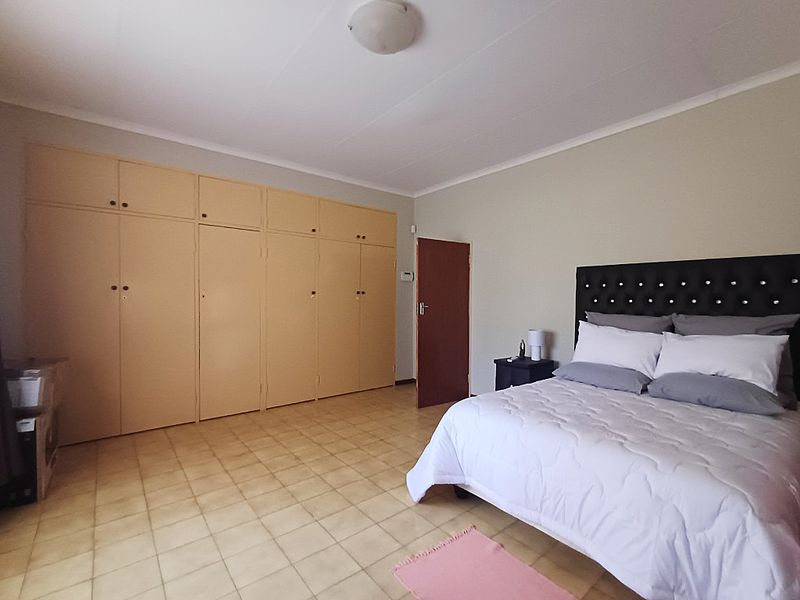 Spacious bedroom featuring extensive built-in cupboards, neutral wall finishes, and durable tiled flooring, offering a functional and well-maintained living space.