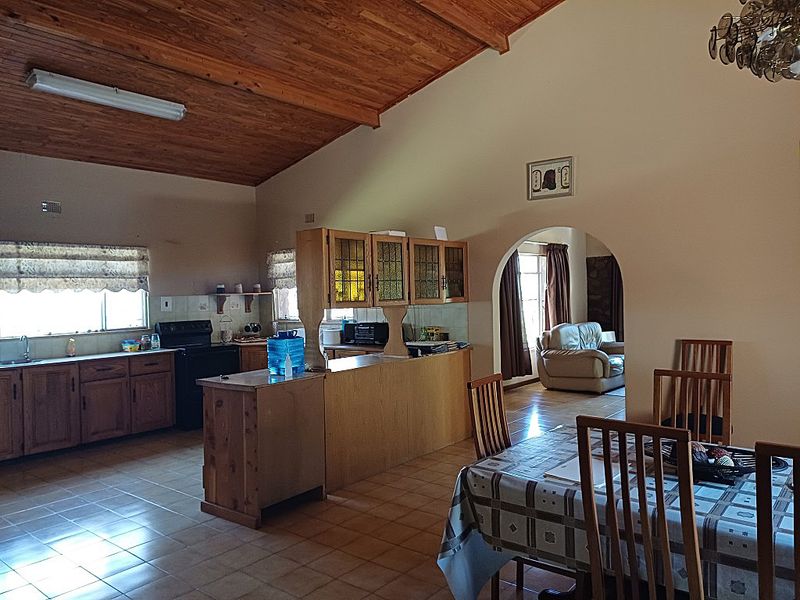 Spacious open-plan kitchen and dining area featuring a vaulted timber ceiling, tiled floors, and traditional wooden cabinetry with a functional layout.