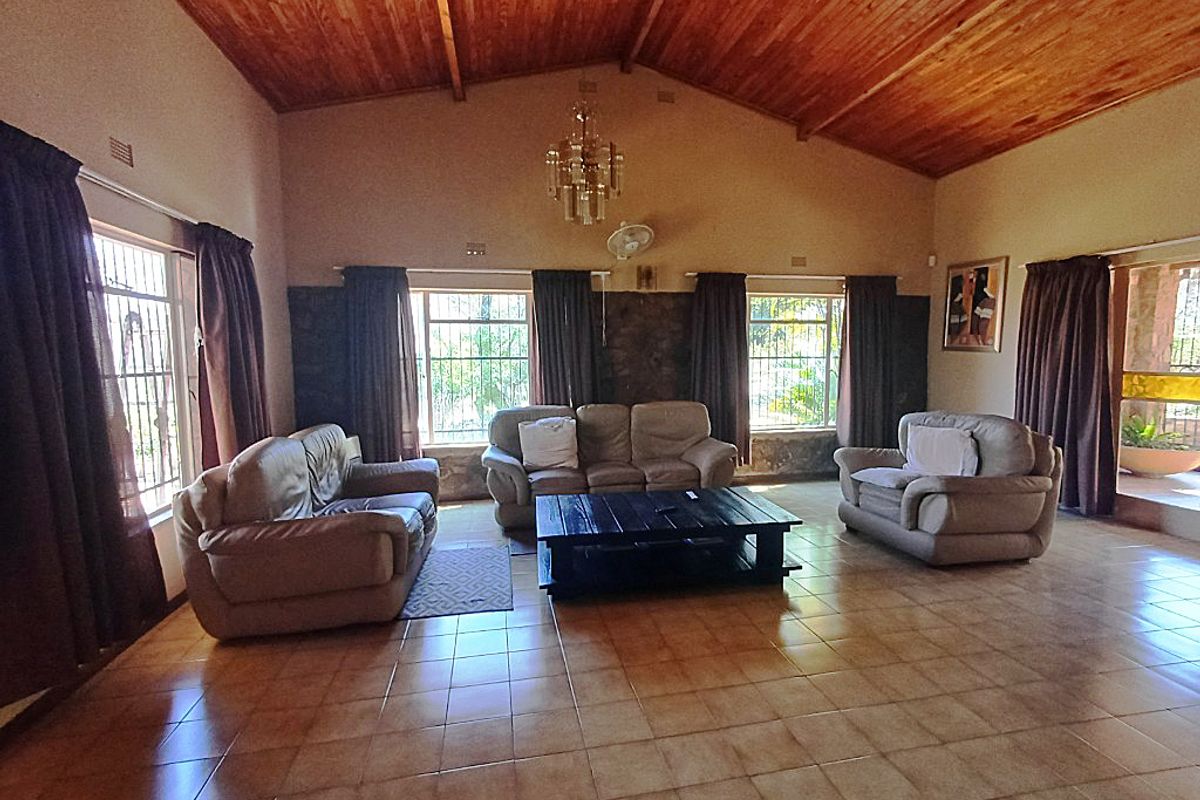 Spacious living room featuring a vaulted timber ceiling, ceramic tiled flooring, and a stone feature wall with large windows and security bars.