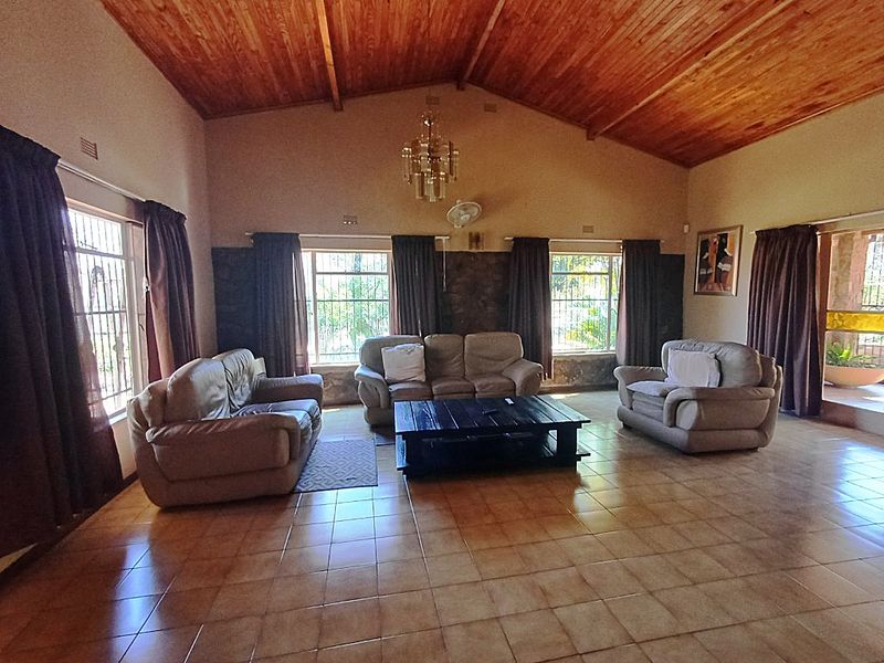 Spacious living room featuring a vaulted timber ceiling, ceramic tiled flooring, and a stone feature wall with large windows and security bars.