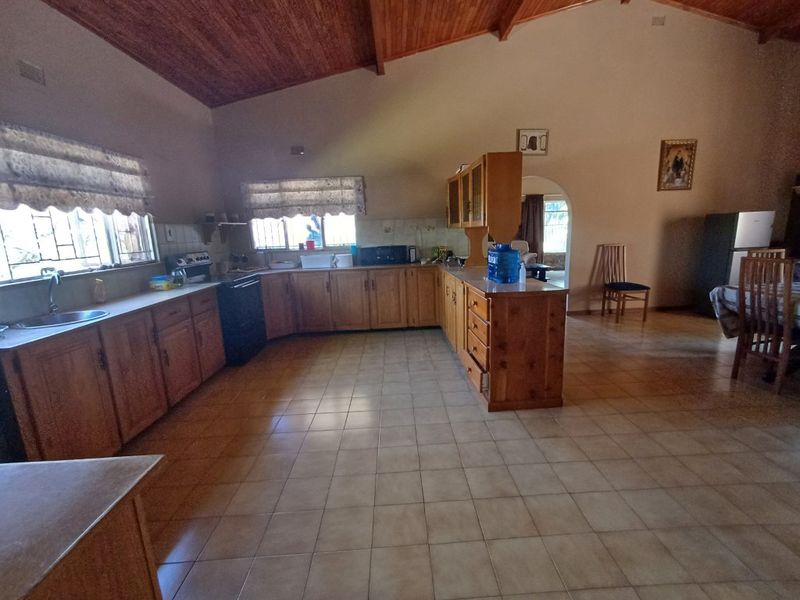 Spacious kitchen featuring wooden cabinetry, a central island, tiled flooring, and a vaulted timber ceiling, offering a functional layout with potential for modernization.