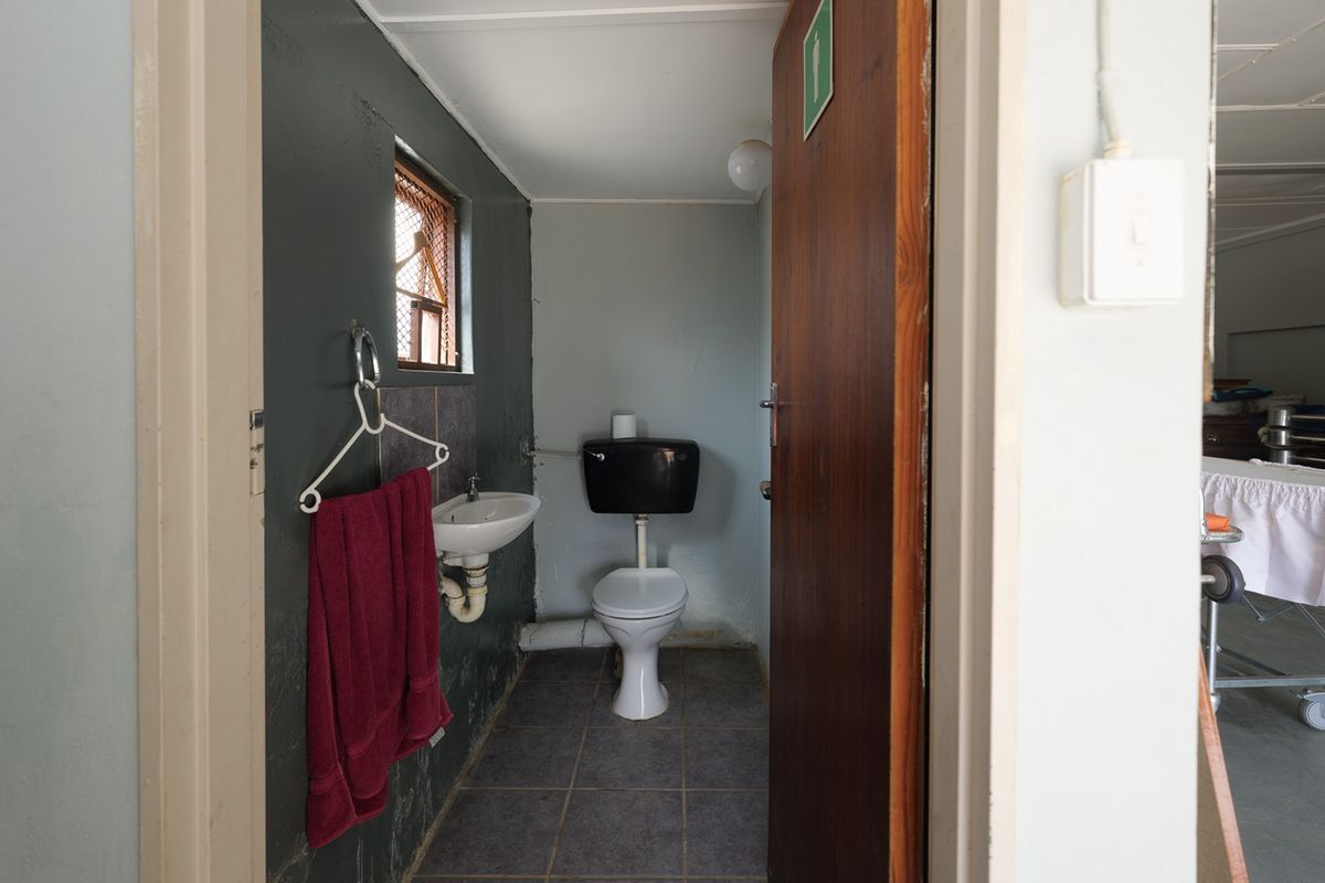 A functional, compact commercial bathroom featuring a wall-mounted basin, toilet, and tiled flooring, requiring cosmetic updates to improve its overall condition.