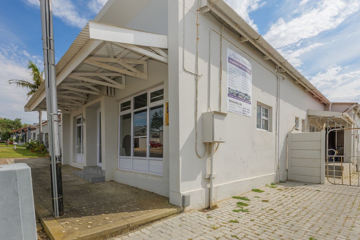 Front exterior view of a commercial property featuring a covered entrance, paved driveway, and security fencing.