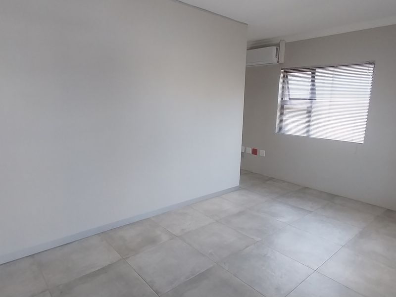 A clean, empty office space featuring neutral tiled flooring, an installed air conditioning unit, and window blinds, providing a versatile professional environment.