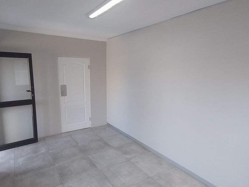 A clean, empty office space featuring neutral walls, tiled flooring, and a combination of internal and external access doors.