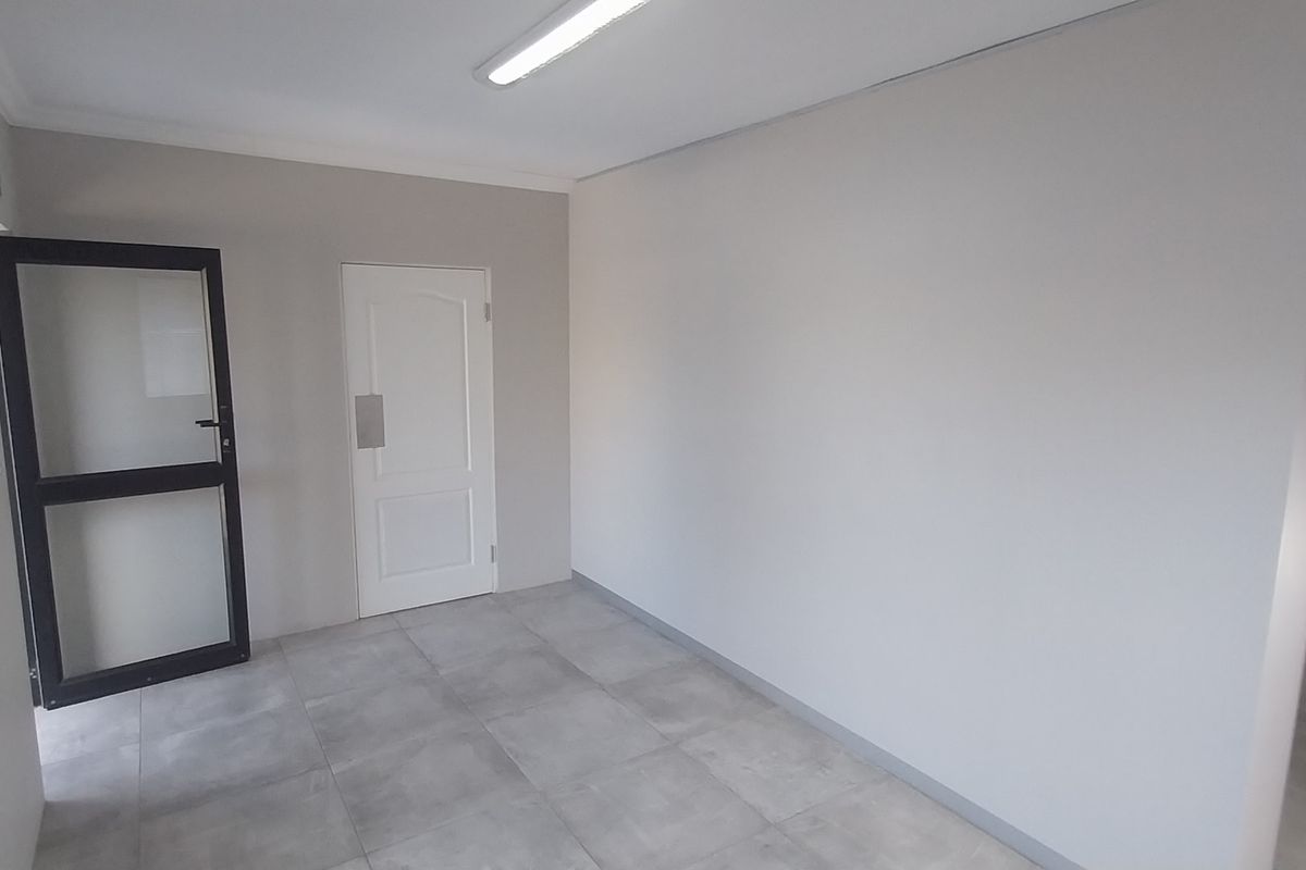 A clean, empty office space featuring neutral walls, tiled flooring, and a combination of internal and external access doors.