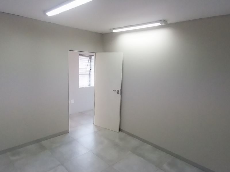 A clean, empty office space featuring neutral walls, tiled flooring, and functional overhead lighting, providing a versatile environment for professional use.