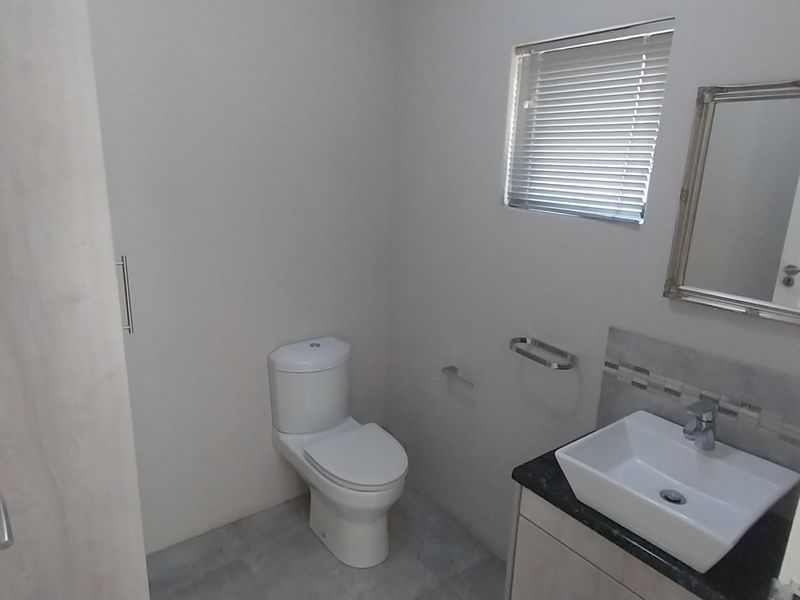 A clean and modern guest bathroom featuring a vessel sink, vanity cabinet, and toilet, finished with neutral wall tones and tiled flooring.