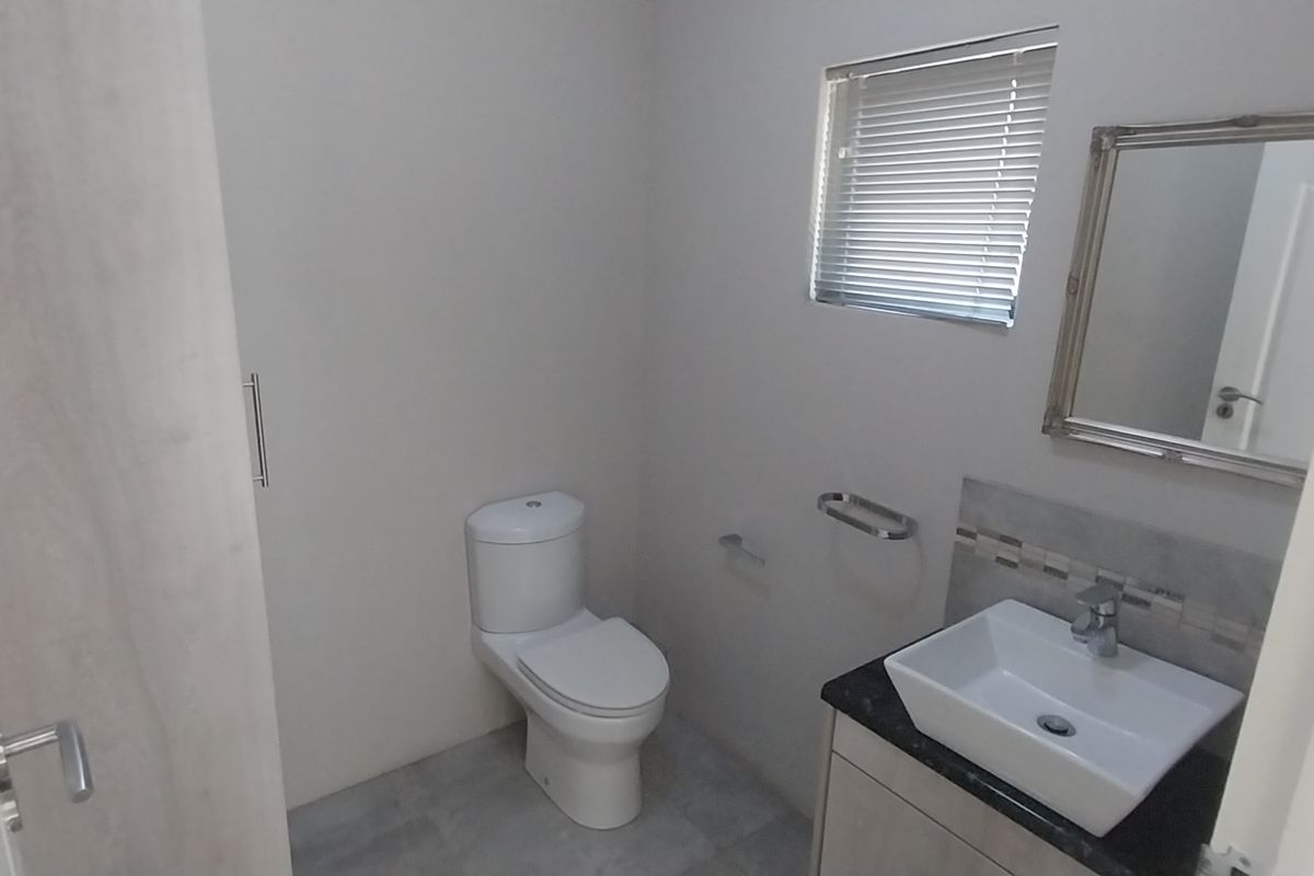 A clean and modern guest bathroom featuring a vessel sink, vanity cabinet, and toilet, finished with neutral wall tones and tiled flooring.