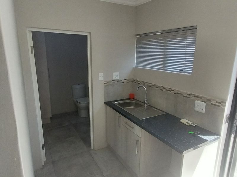 A clean, functional scullery area featuring built-in cabinetry, a stainless steel sink, and direct access to an outdoor paved area.