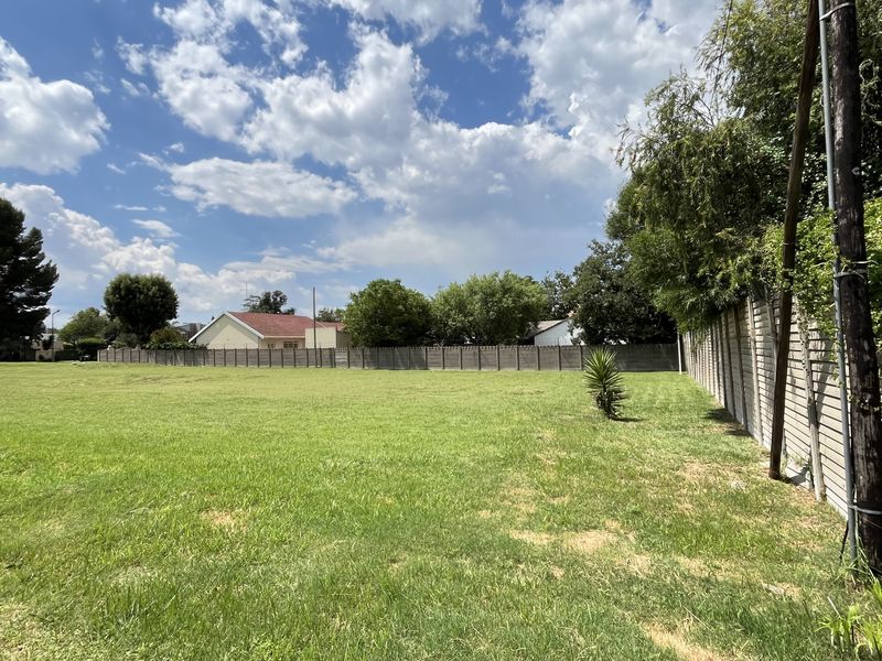 A wide-angle view of a vacant commercial land plot featuring a grass lawn and perimeter concrete boundary walling.