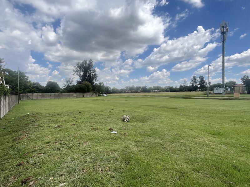 A wide, level vacant commercial plot featuring perimeter concrete walling and clear access, suitable for development.