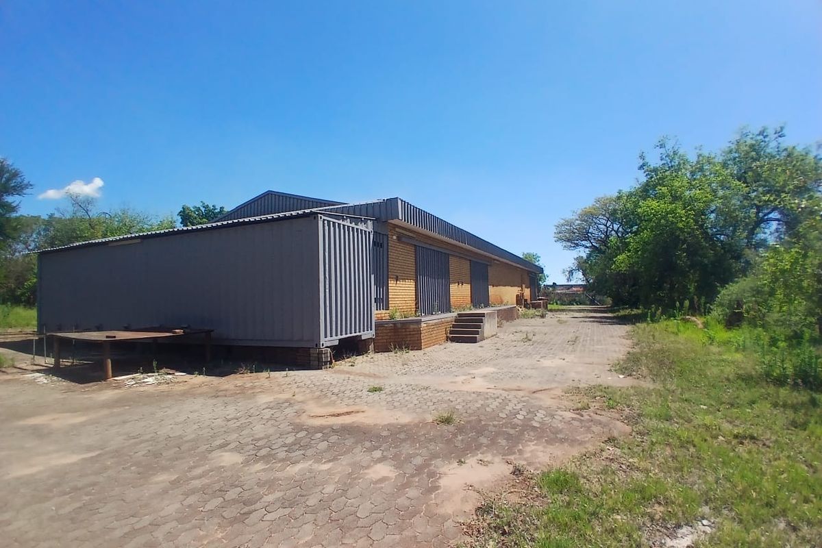 Rear view of an industrial property featuring a brick building, metal roofing, a concrete loading dock, and a large paved yard area.