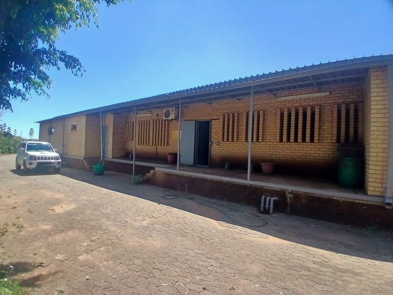 Industrial property featuring a face brick facade with a covered veranda, paved driveway, and exterior air conditioning unit.