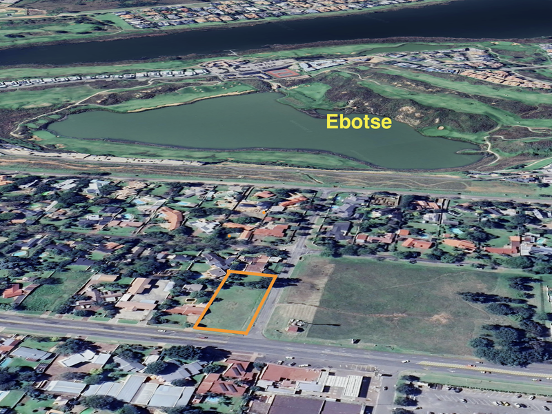 Aerial view of a vacant commercial land plot highlighted in orange, situated in a developed residential and commercial area near Ebotse.