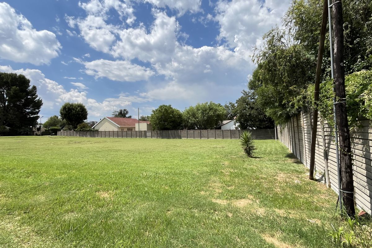 A wide-angle view of a vacant commercial land plot featuring a grass lawn and perimeter concrete boundary walling.