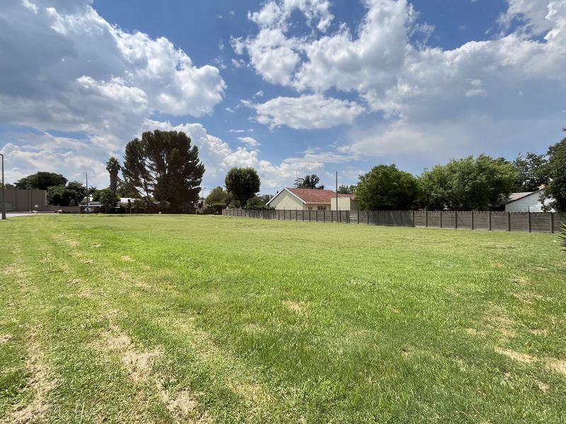 A wide-angle view of a vacant commercial land plot featuring well-maintained grass, perimeter fencing, and street-side access.