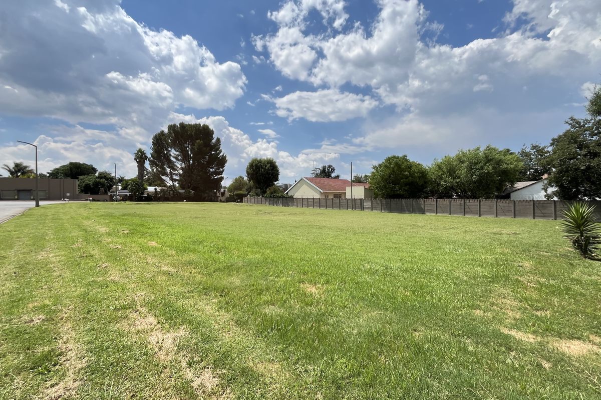 A wide-angle view of a vacant commercial land plot featuring well-maintained grass, perimeter fencing, and street-side access.