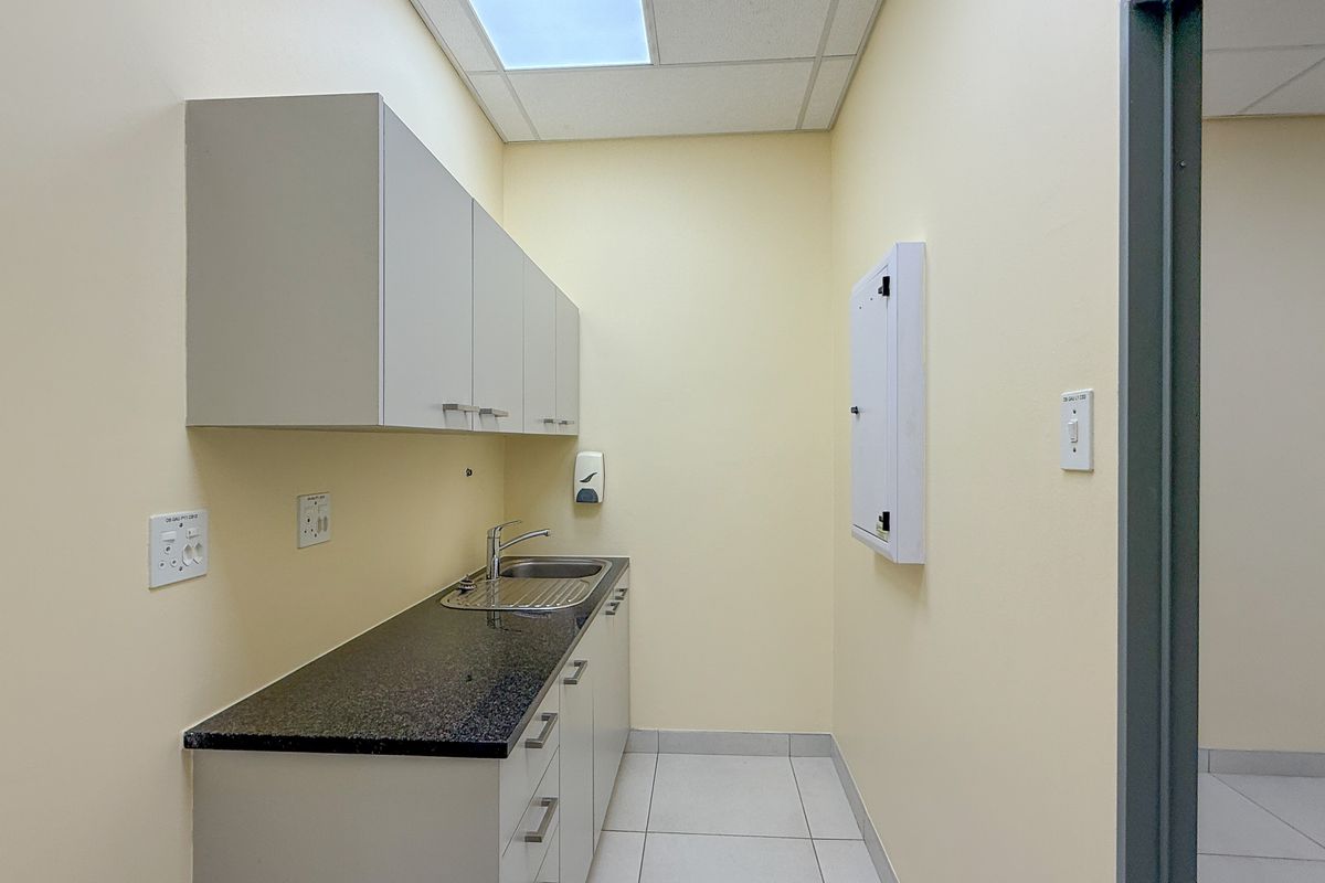 A functional kitchenette area featuring built-in cabinetry, a granite countertop, a stainless steel sink, and a drop ceiling with integrated lighting.