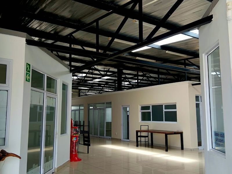 Spacious open-plan commercial interior featuring high exposed steel roof trusses, abundant natural light from skylights, and modern tiled flooring with glass partition offices.