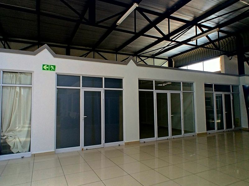 Spacious commercial open-plan area featuring high exposed steel roof trusses, polished tiled flooring, and multiple glass-partitioned office or retail units.