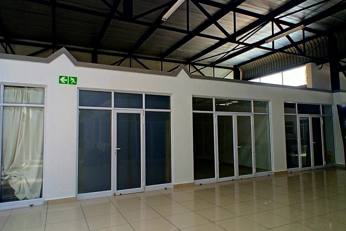Spacious commercial open-plan area featuring high exposed steel roof trusses, polished tiled flooring, and multiple glass-partitioned office or retail units.