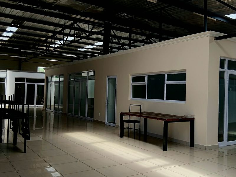 Spacious open-plan commercial interior featuring high exposed steel ceilings with skylights, polished tiled flooring, and modern aluminium-framed glass office partitions.