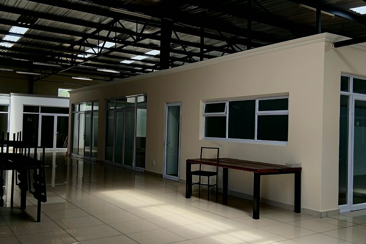 Spacious open-plan commercial interior featuring high exposed steel ceilings with skylights, polished tiled flooring, and modern aluminium-framed glass office partitions.