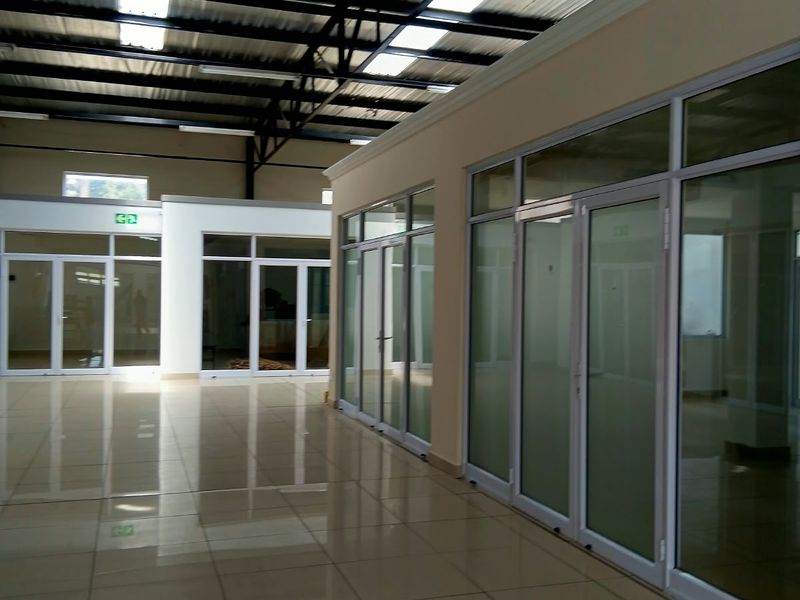 Spacious commercial office interior featuring polished tile flooring, modern glass partitioning, and an open-plan layout with high exposed ceilings and natural skylight illumination.